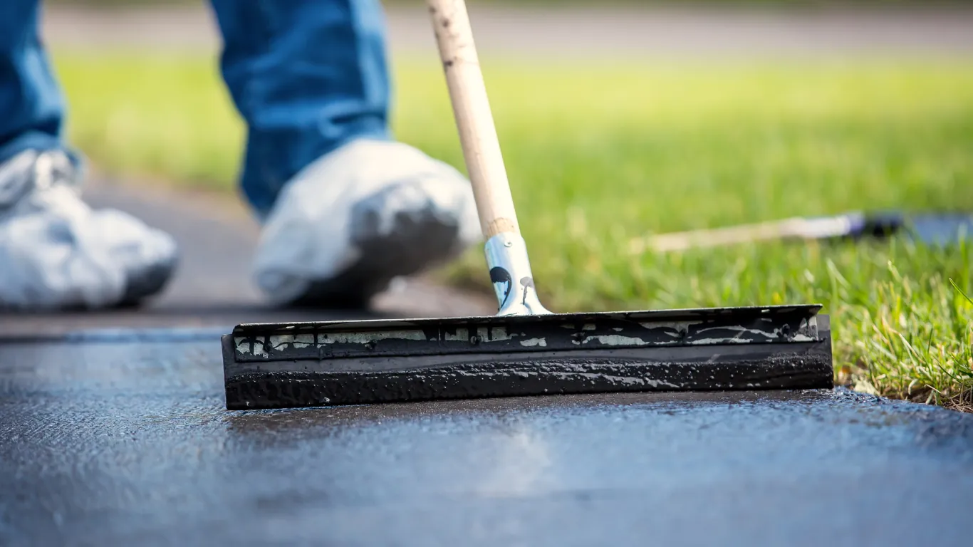Fresh black sealer being pulled across an asphalt driveway with a squeegee